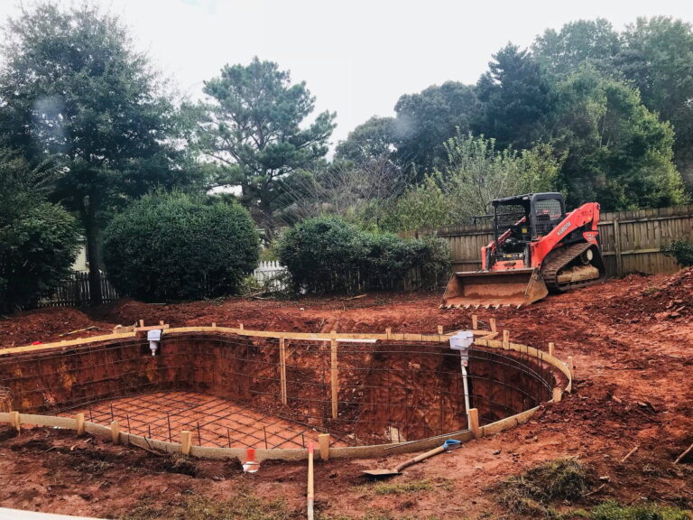 A backyard under construction with an in-ground pool being built—showcasing the best time to build a pool—surrounded by dirt, wooden framing, and a bulldozer parked nearby.