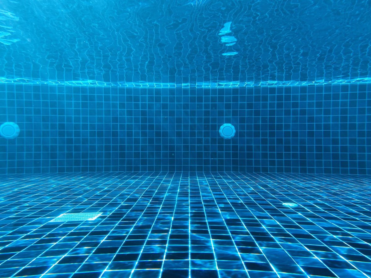 Underwater view of a swimming pool showing blue tiles, pool drains, and light reflections on the water and pool floor—a scene that highlights the importance of fall pool maintenance to keep your pool sparkling clean.