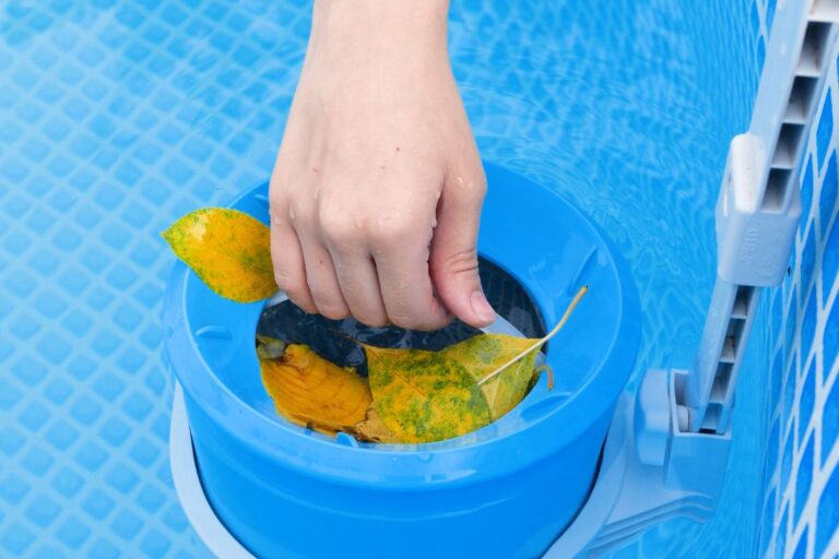 A hand removes yellow leaves from a blue pool skimmer basket in a swimming pool, an essential step before learning how to adjust pool skimmer suction for optimal cleaning.