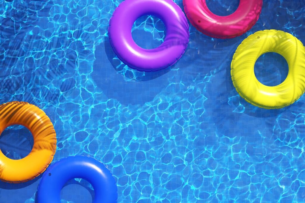 Five colorful inflatable pool rings float on the surface of a clear blue swimming pool in bright sunlight—capturing a moment of pure summer fun and making you wonder what I wish I knew before building a pool.