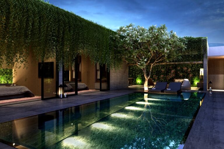 Modern outdoor pool area at dusk with lounge chairs, a large tree, hanging greenery, and open rooms facing the water—highlighted by stylish pool lighting ideas that create a welcoming ambiance.