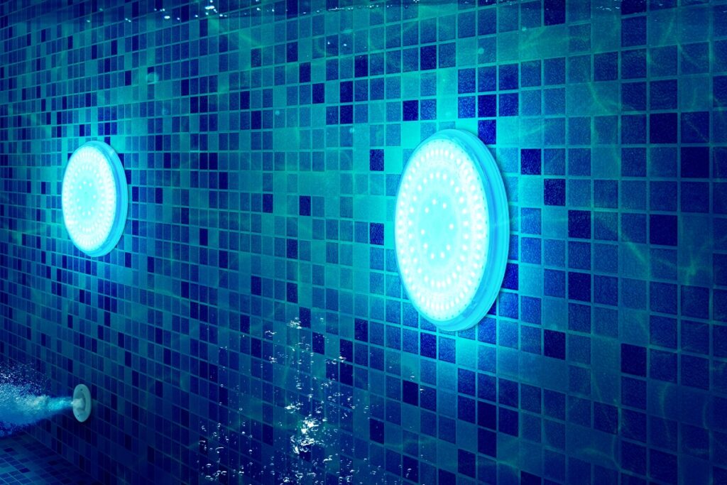 A person is swimming in a blue tiled pool with pool lighting ideas.