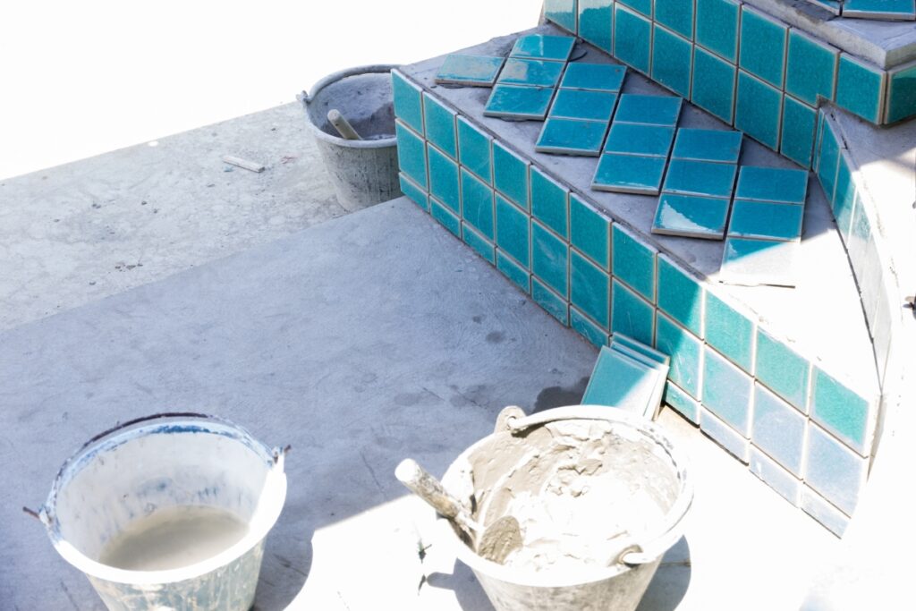 A man is laying tiles in a pool shape on a concrete floor.