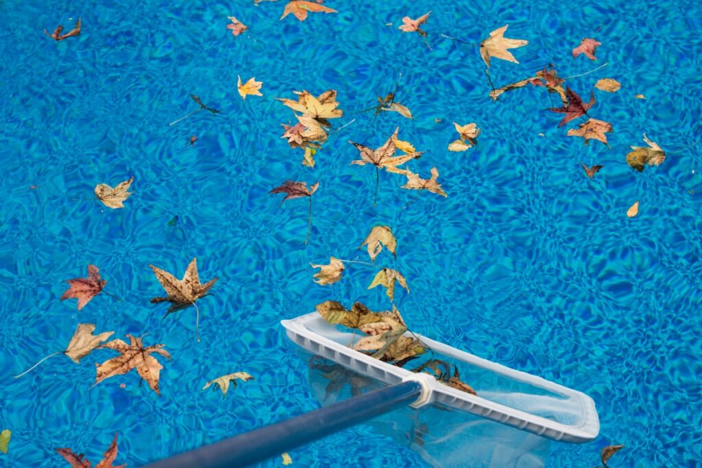 A person closing a pool for winter with a rake.