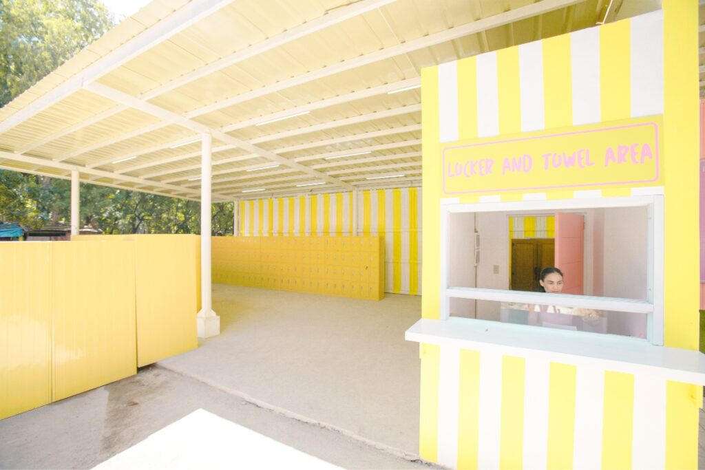 A yellow and white pool cabana with a woman standing in front of it.