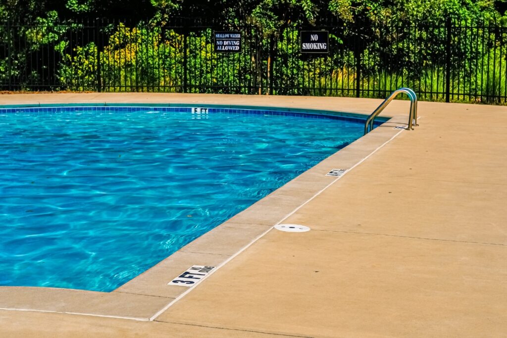 A swimming pool with a fence around it, featuring a durable pool deck material.