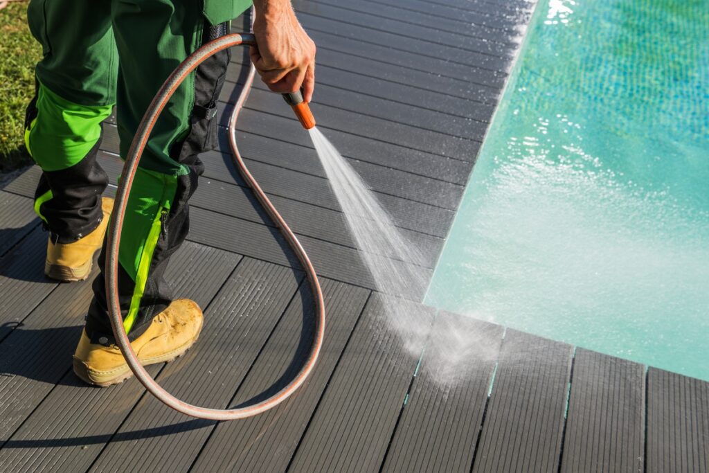 A man using a hose to clean the pool deck.