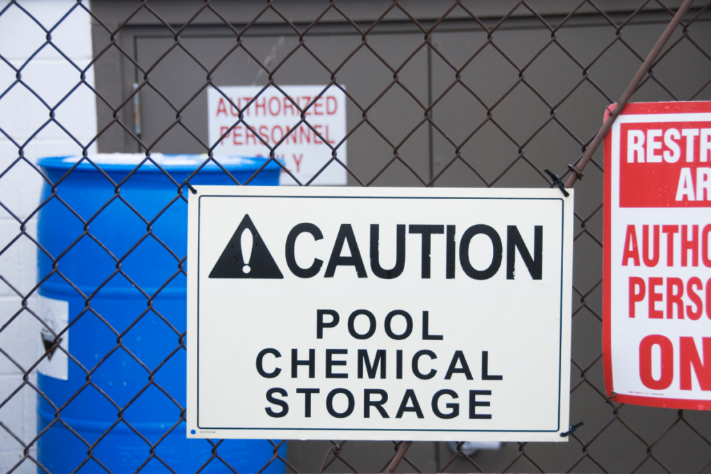 Pool chemical storage signs on a chain link fence.