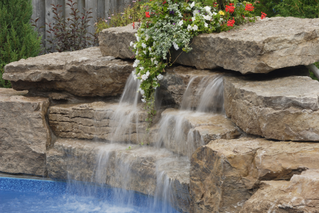 A modern waterfall cascading over rocks amidst a vibrant display of flowers and a pool.