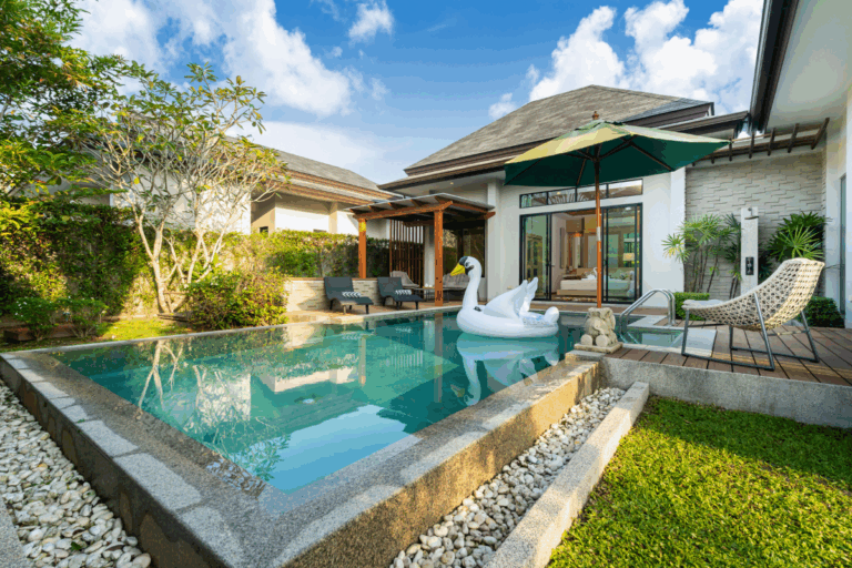 Modern backyard with a small rectangular swimming pool, a swan pool float, lounge chairs under an umbrella, and a patio beside a single-story house—perfect inspiration for modern pool landscaping ideas.