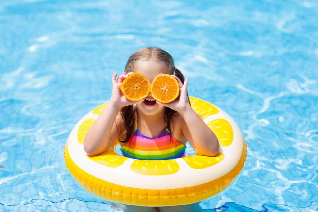 A little girl holding an orange ring in a swimming pool.