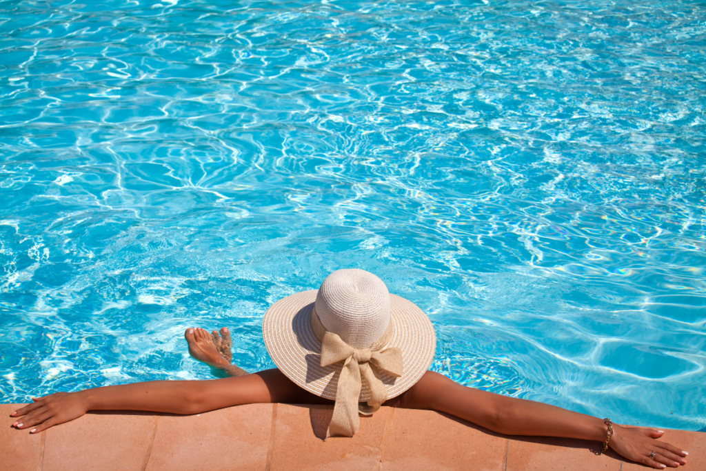 A woman wearing a hat enjoys the relaxation offered by smart pool technology at the edge of a swimming pool.