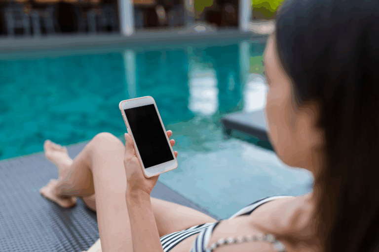A person in a striped swimsuit is lounging by a poolside on a chair, holding a smartphone with a blank screen—perhaps ready to explore the latest in smart pool technology.