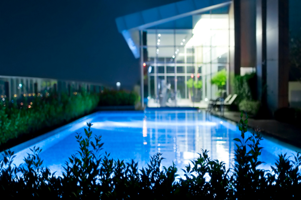Illuminated outdoor pool at night with modern lighting and a contemporary building in the background.