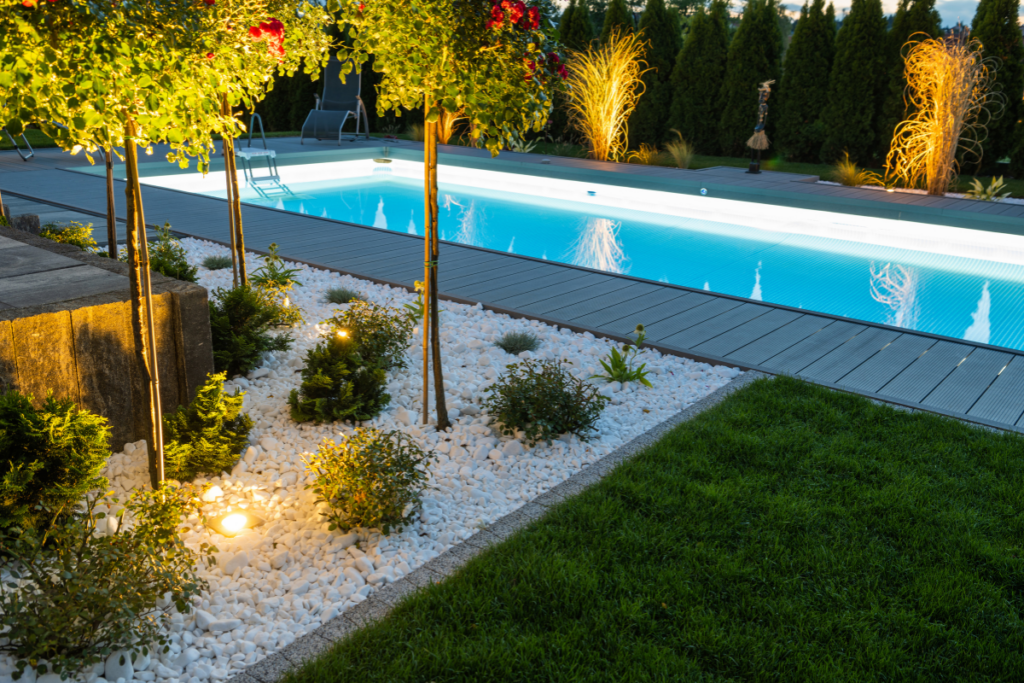 Illuminated backyard garden with an outdoor swimming pool at dusk.