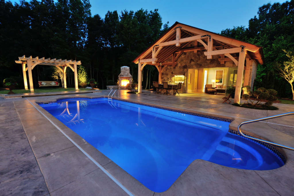 Illuminated backyard pool area with outdoor lighting, a pergola, and outdoor living space at dusk.