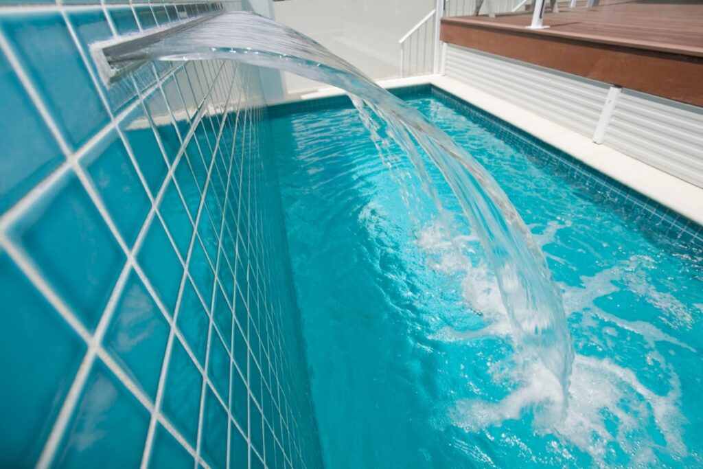 Water cascades from a spout into an inground pool lined with blue tiles, creating one of the most serene water features you could imagine.