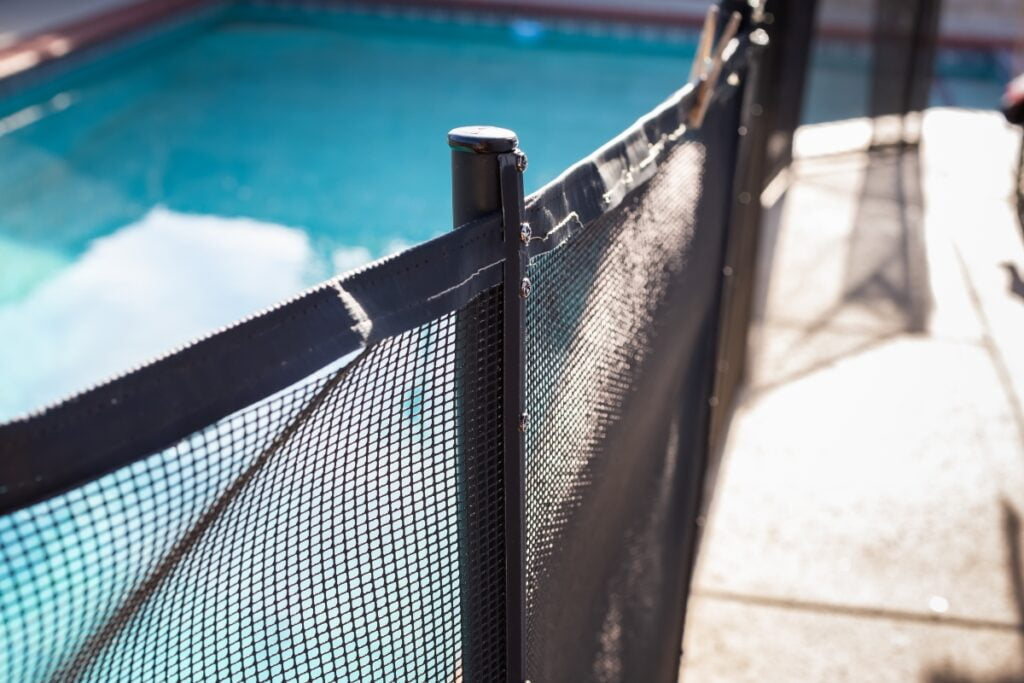 Close-up of a black mesh safety fence adhering to pool safety regulations, with focus on the metal post and mesh texture, under clear sunlight.