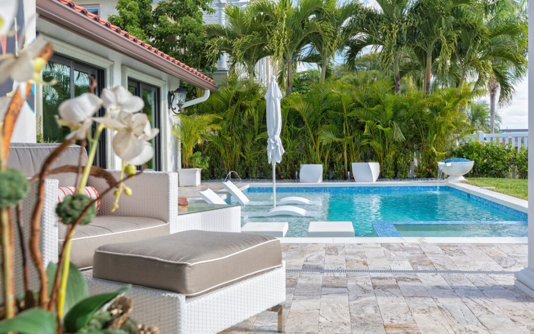 Luxury backyard pool area with lounge chairs, umbrella, and tropical plants. Outdoor poolside decor complements the modern house with large windows visible in the background.