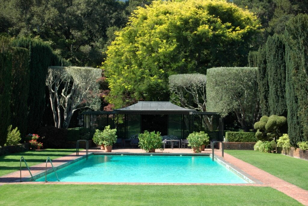 A well-manicured garden with a large rectangular swimming pool, surrounded by trees and shrubs, offers a serene spot for poolside gardening. A charming gazebo sits in the background.