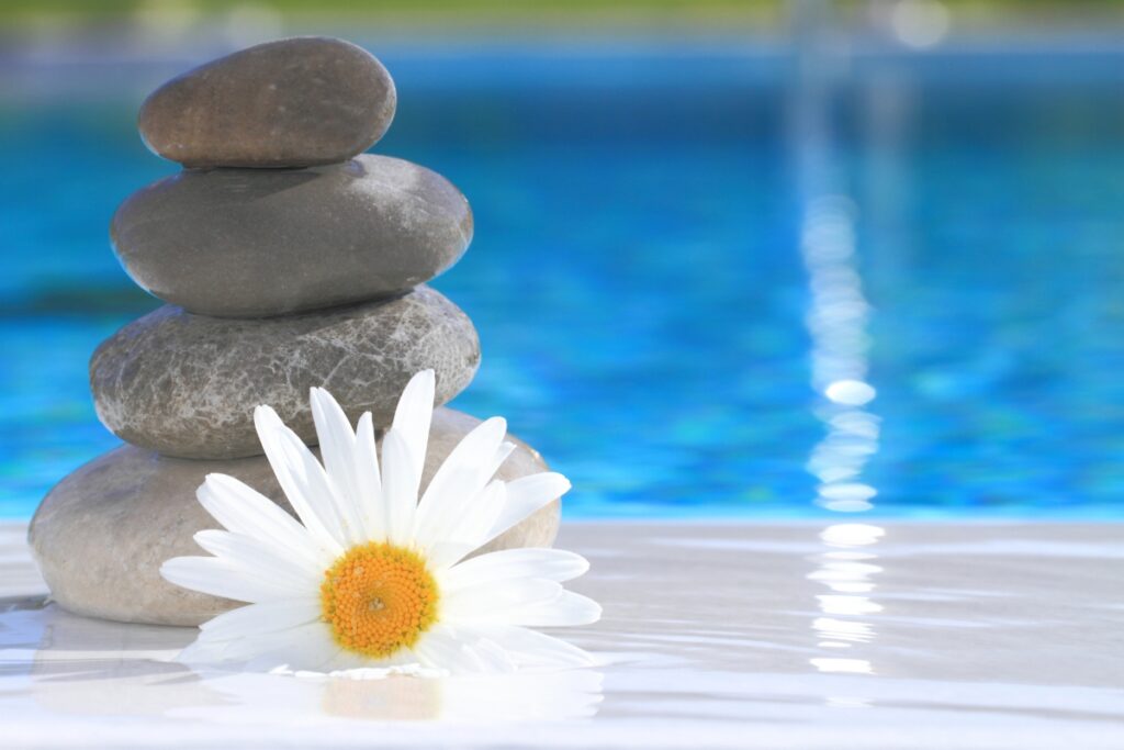 Stacked smooth stones and a white daisy flower are placed next to a clear blue pool, creating an idyllic setting for contemplating privacy solutions.