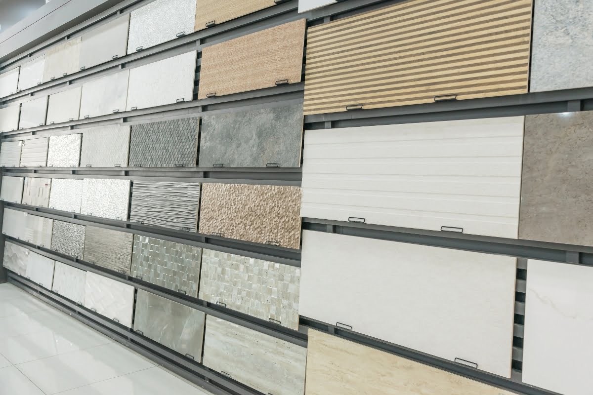 A display wall showcasing a variety of ceramic tiles in different colors, textures, and patterns, arranged in rows inside the showroom, also includes options that can double as patio decking material.