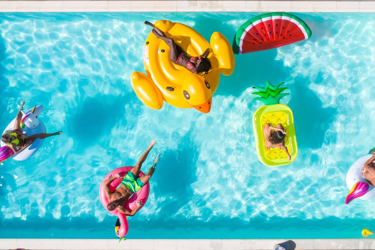 Four people relax on inflatable rafts shaped like a duck, watermelon, flamingo, and pineapple in a clear blue swimming pool, perfect for enjoying after following some essential pool renovation tips.