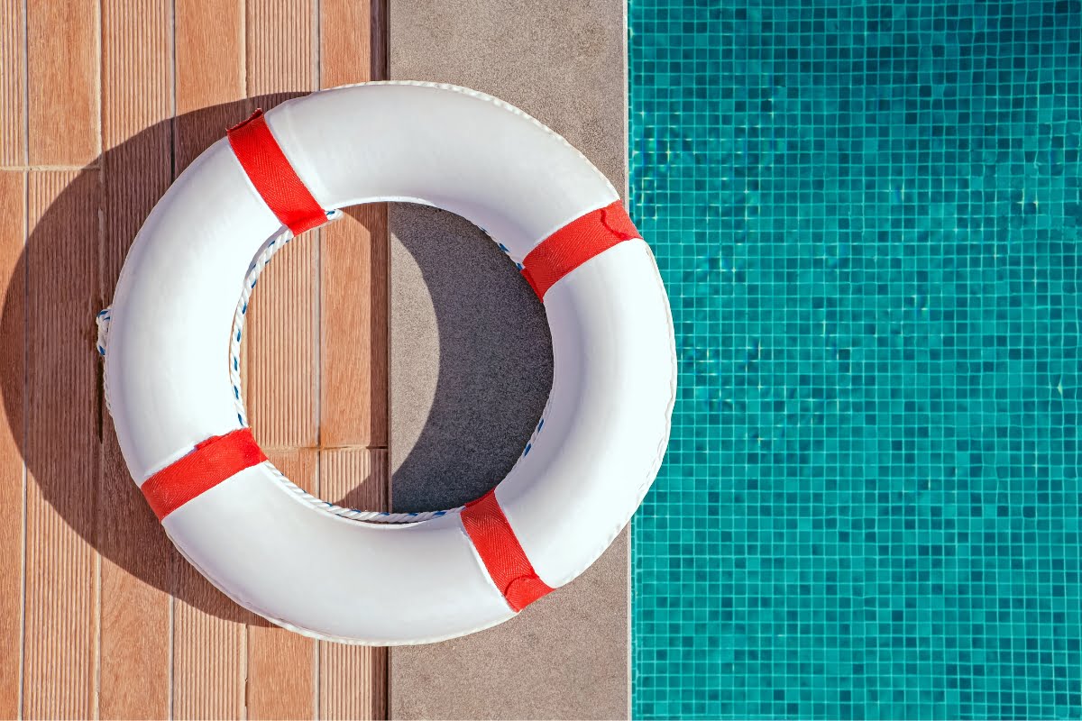 A white lifebuoy with red straps is placed on the edge of a tiled swimming pool, offering both safety and a classic touch, perfect for those looking for pool renovation tips.