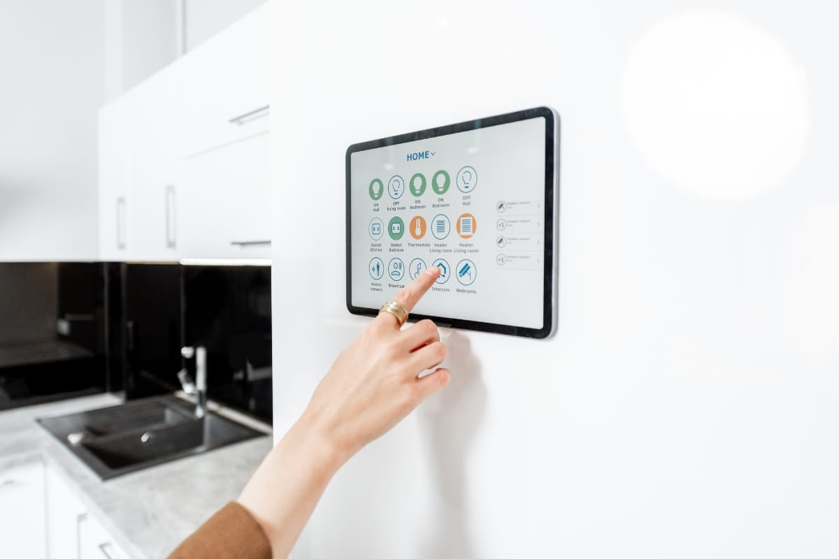 A hand interacts with a wall-mounted smart home control panel in a modern kitchen, selecting an option on the touchscreen, reminiscent of accessing features in a gym with pool setting.