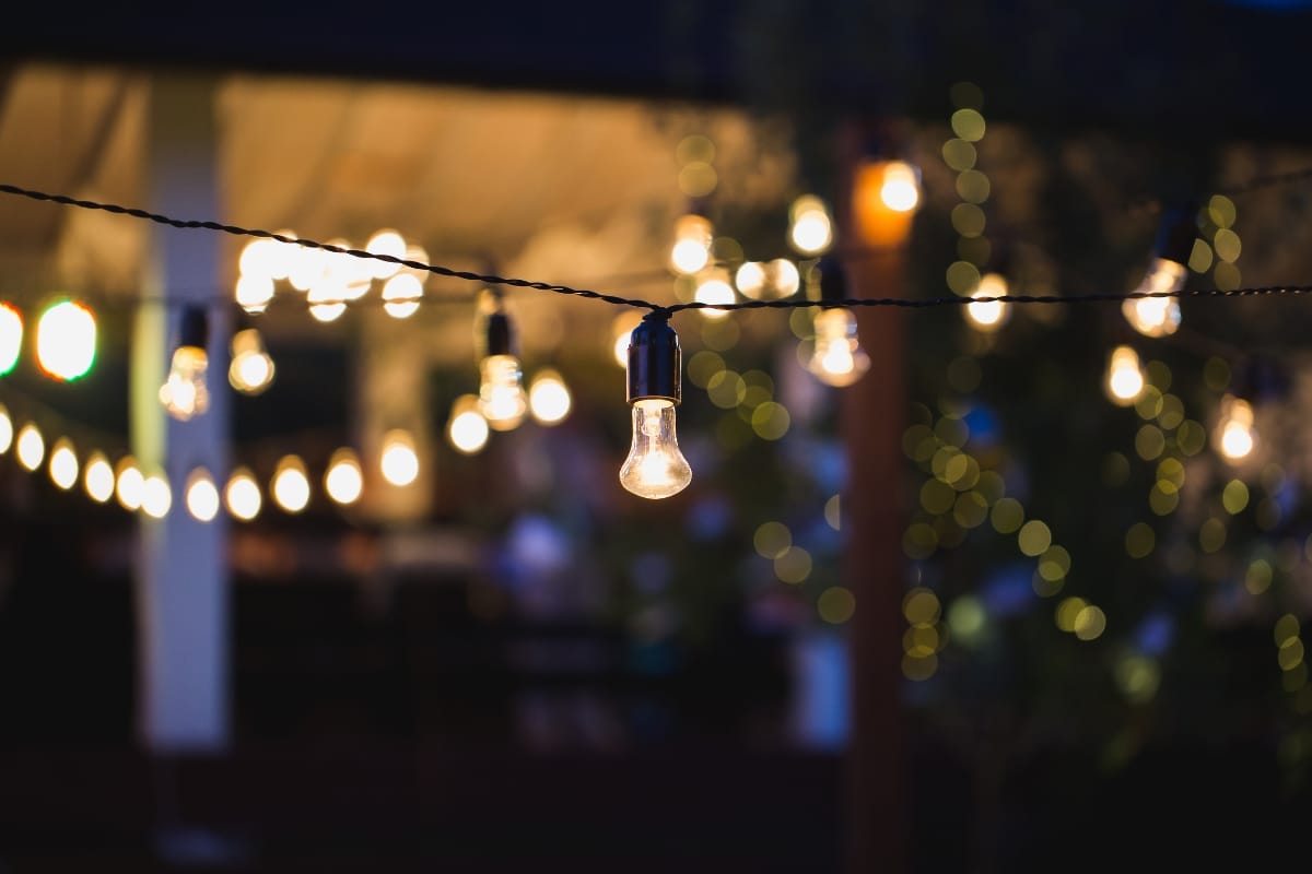 String of exposed light bulbs hanging outdoors at night, their warm glow enhancing the poolside charm with a bokeh effect of blurred lights in the background, inviting you to ignite your imagination with captivating fire pit ideas.