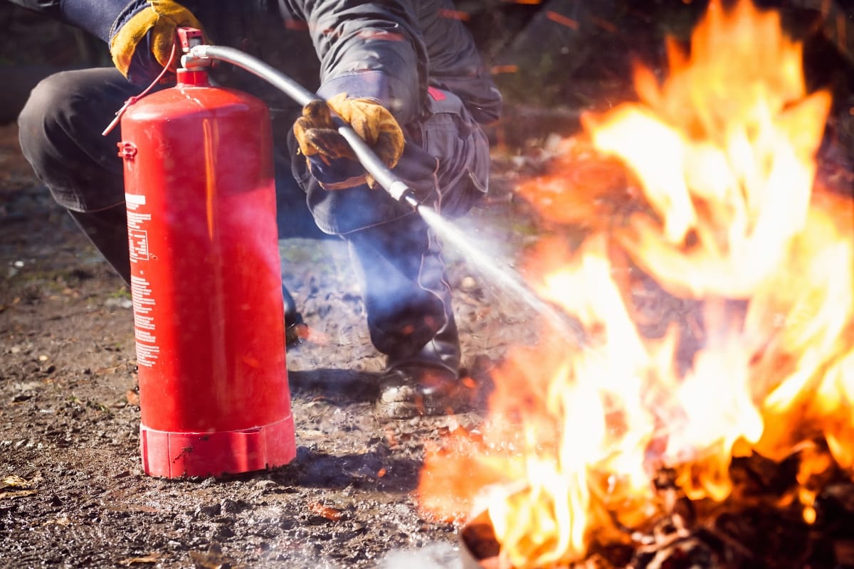 A person is skillfully using a red fire extinguisher to put out the flames near an outdoor fire pit, showcasing impressive fire pit ideas in action.