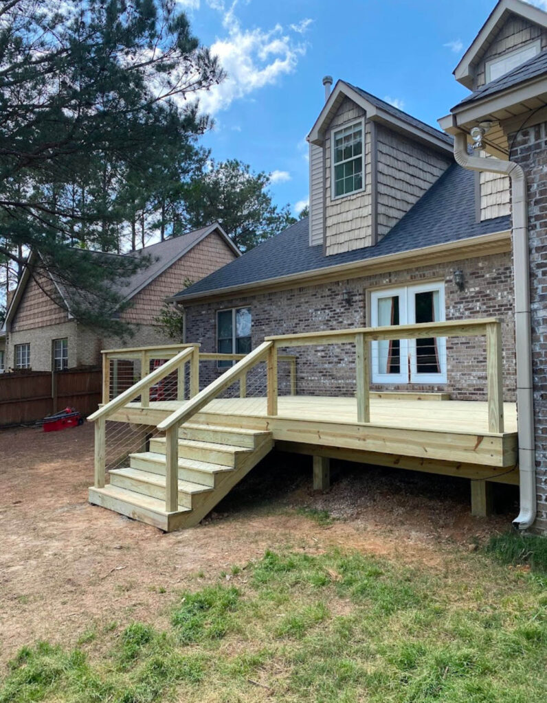A wooden deck with stairs and railings, typical of many inviting patios and decks, extends from the back of a brick house into the backyard.