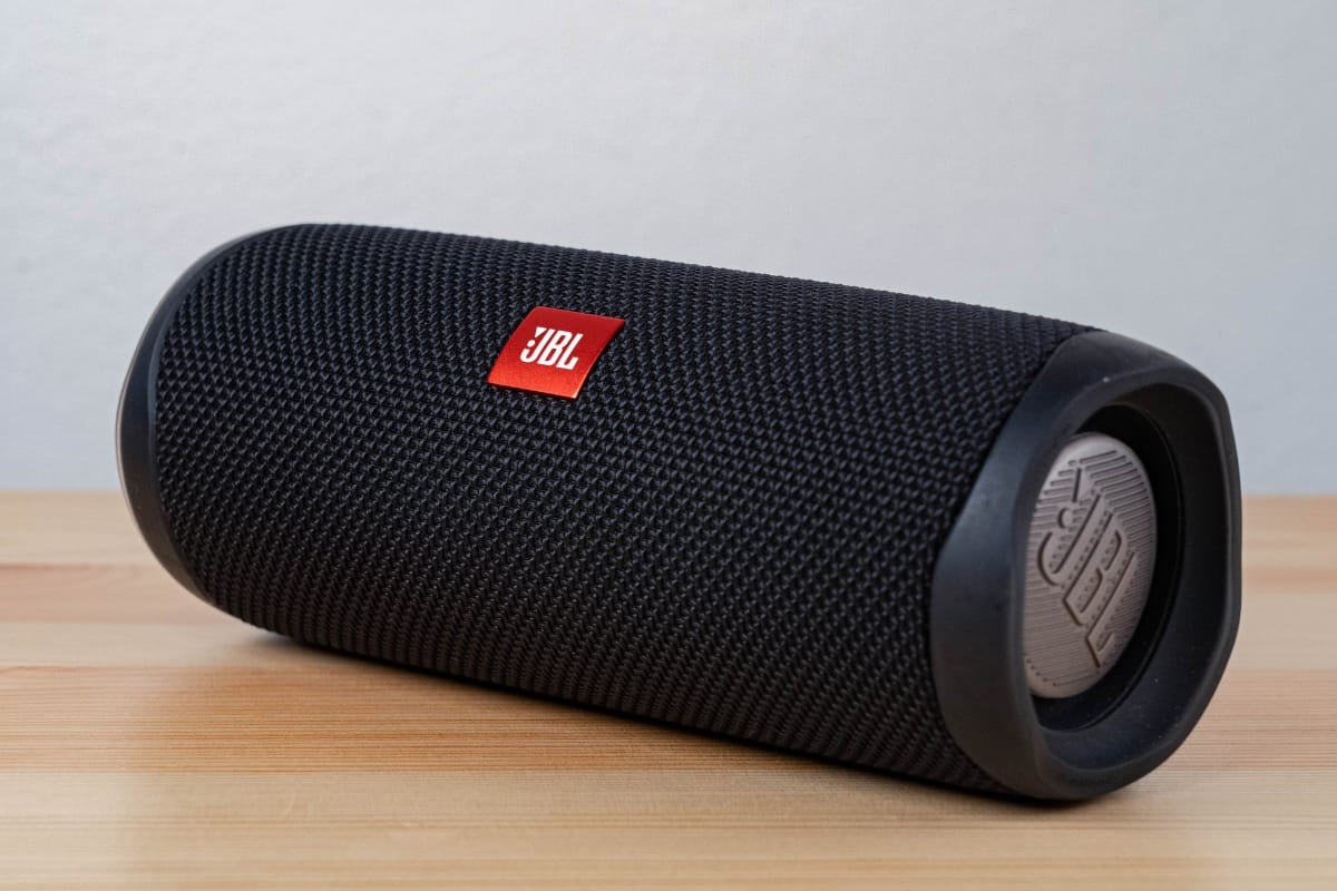 A black JBL portable Bluetooth speaker sits on a light wooden surface, making it one of the best pool accessories with its textured grille and logo visible.