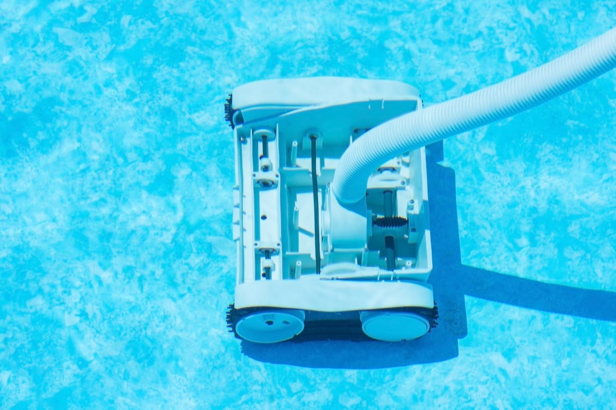 A robotic pool cleaner moves across the floor of a bright blue swimming pool, attached to a hose, offering effortless cleaning and smart pool maintenance tips for a sparkling swim.