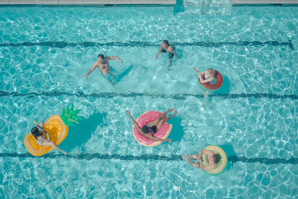 Six people in a swimming pool, seen from above, float on colorful inflatable fruit-shaped rings—enjoy carefree fun while keeping the water sparkling with simple pool maintenance tips.