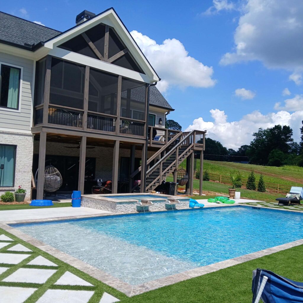 A modern house with a screened-in porch, outdoor staircase, and a rectangular inground swimming pool features expert landscape design installation in the landscaped backyard on a sunny day.