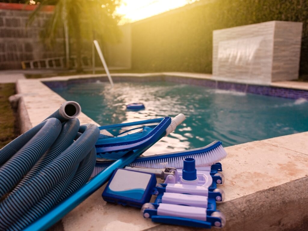 Pool cleaning tools, including a vacuum hose, brush, and net, are placed on the poolside next to an outdoor swimming pool in a Dawsonville backyard—perfectly set for maintenance or before a pool renovation at the best timing.