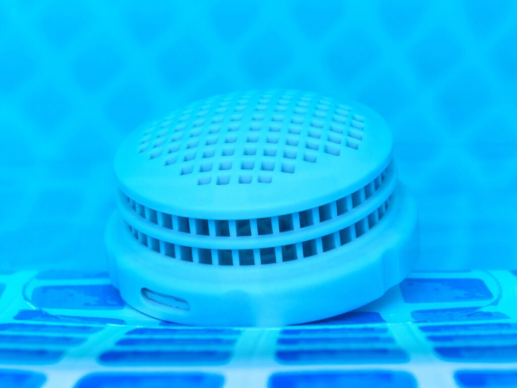 Close-up of a round, vented plastic object with a grid pattern, placed on blue and white tiles, possibly submerged in water—a key accessory to help winterize your pool.