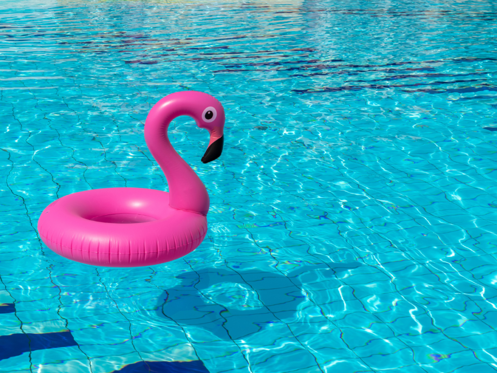 A pink inflatable flamingo float is drifting in a clear blue swimming pool with sunlight reflecting on the water, ready for some fun pool games.