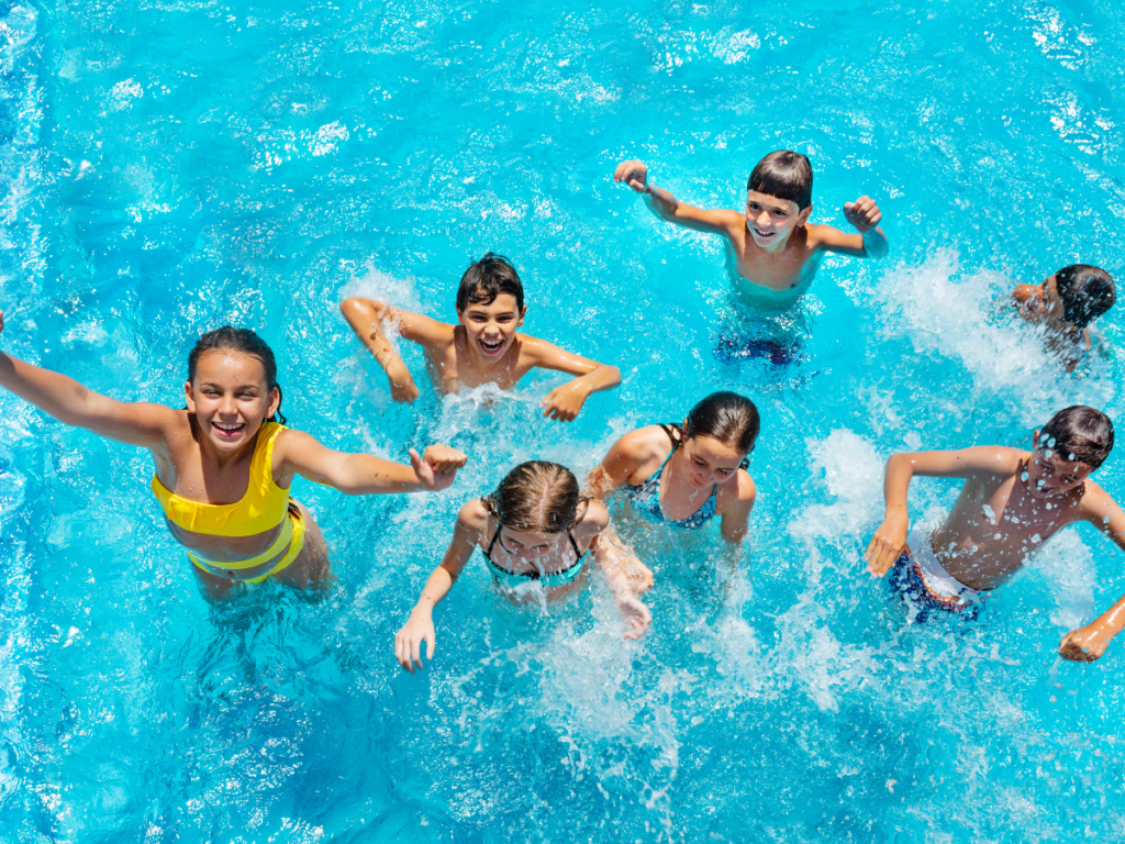 A group of children play pool games and splash in a swimming pool on a sunny day.