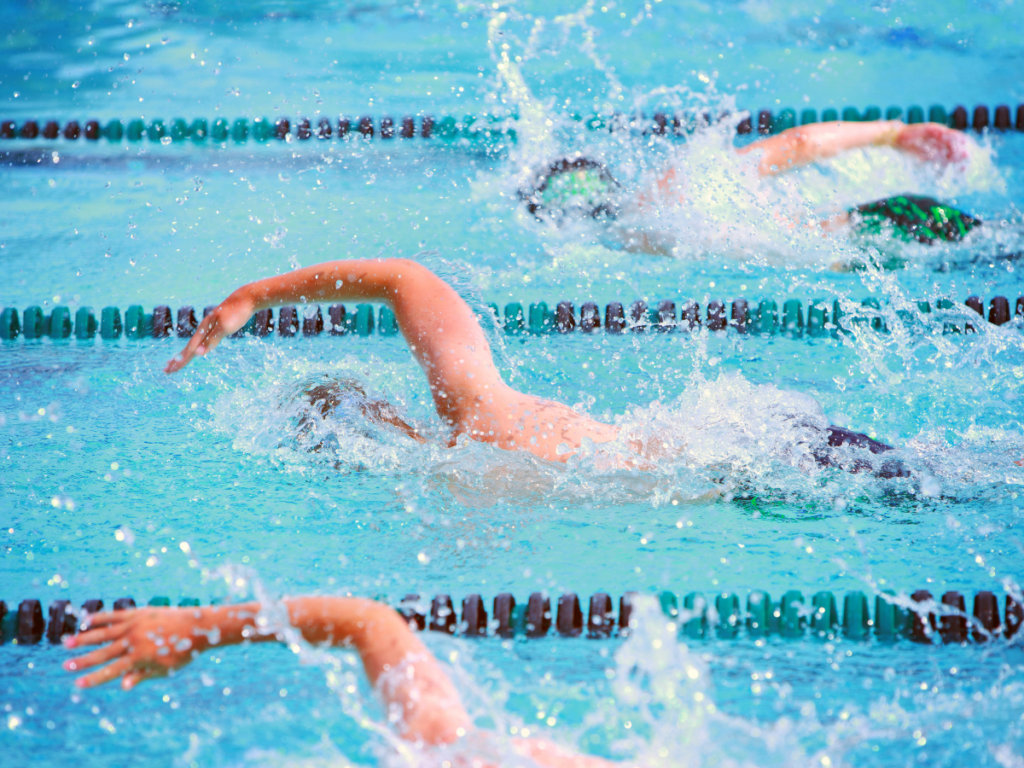 Three swimmers compete in a freestyle race in a pool, creating splashes as they move through the water in separate lanes during exciting pool games.