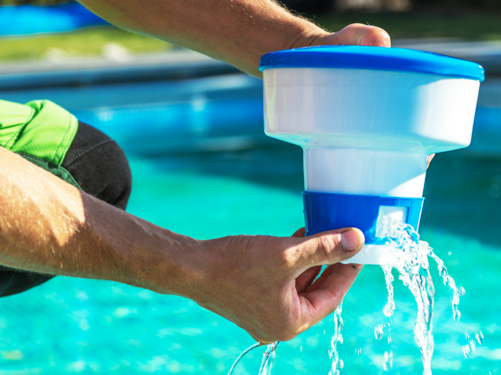 Person holding a blue and white pool chemical dispenser with water flowing from it by the edge of a swimming pool, preparing for effective pool stain removal.